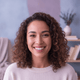 Headshot of a smiling woman in her late 20s, with a blurred background of soft blue and lilac tones.