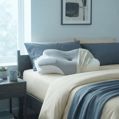 KaizenSleep ergonomic memory foam pillow on a bed with slate blue and cream linens in a modern bedroom.