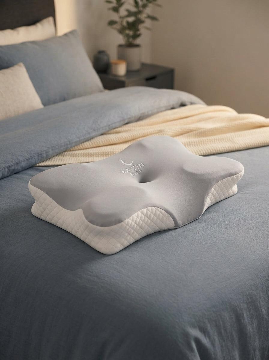 KaizenSleep ergonomic memory foam pillow resting on a bed with slate blue and cream bedding in a modern bedroom.